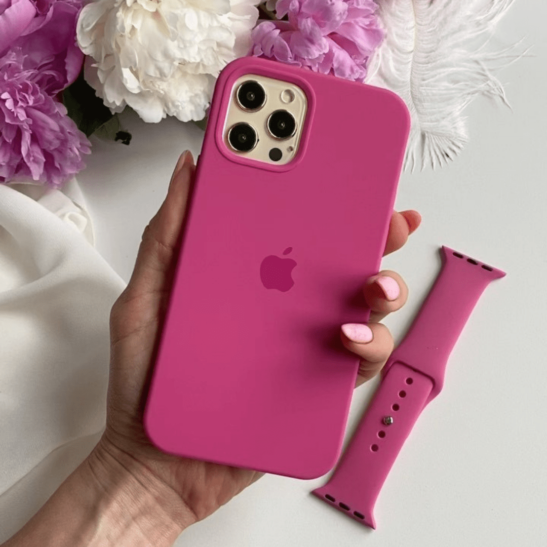 Hand holding a pink phone case with an Apple logo, next to a matching pink watch strap on a light background with flowers.